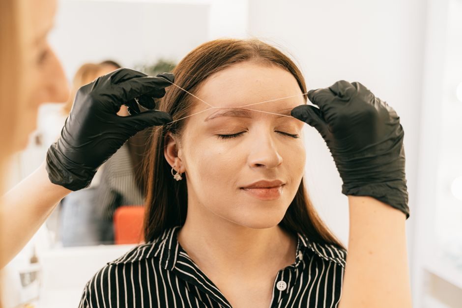 A woman with her eyes closed having her eyebrows threaded