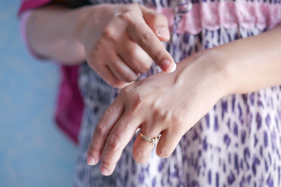 A person applying moisturizer to their hand and arm
